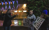 People protesting outside holding signs saying "sign the petition" and "free water" as another person defensively points their finger at them.